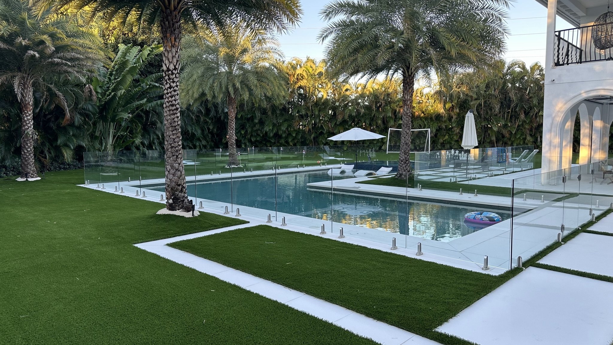 Finished turf lawn around a swimming pool, with palms and a bright residential patio